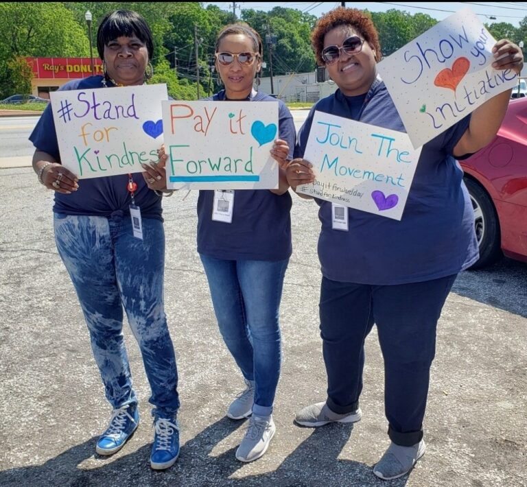 Three people holding kindness posters outdoors.